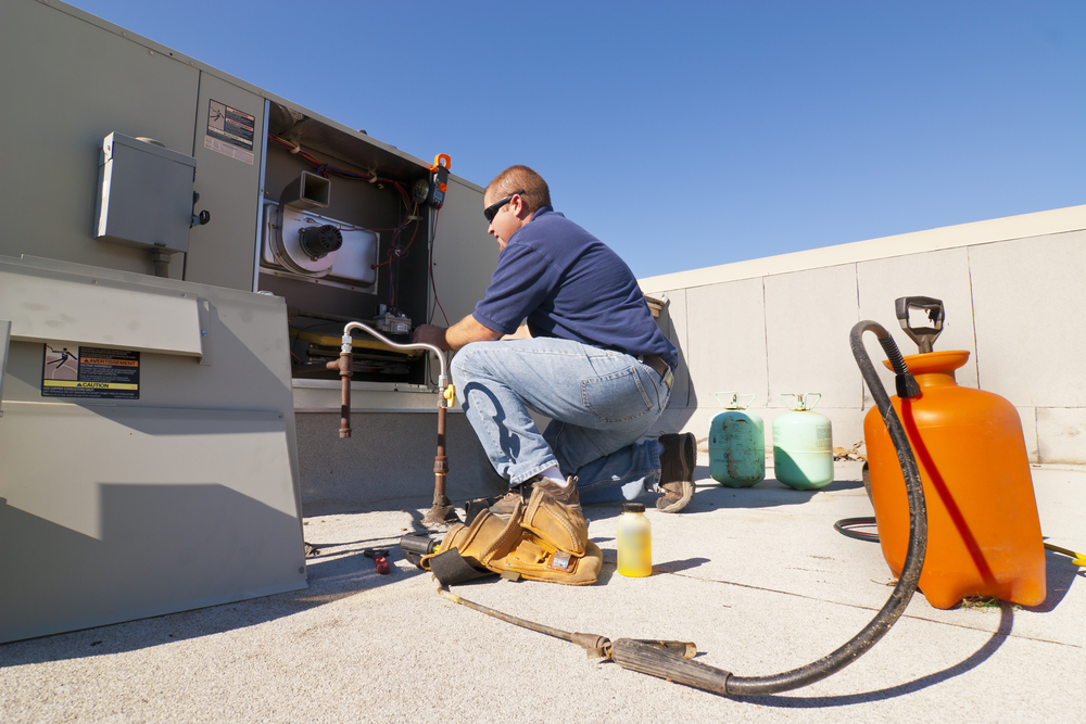 A man wearing sunglasses works on an air conditioning system from a roof