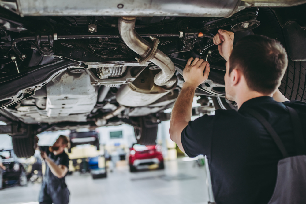 Two men work on the underside of a car.